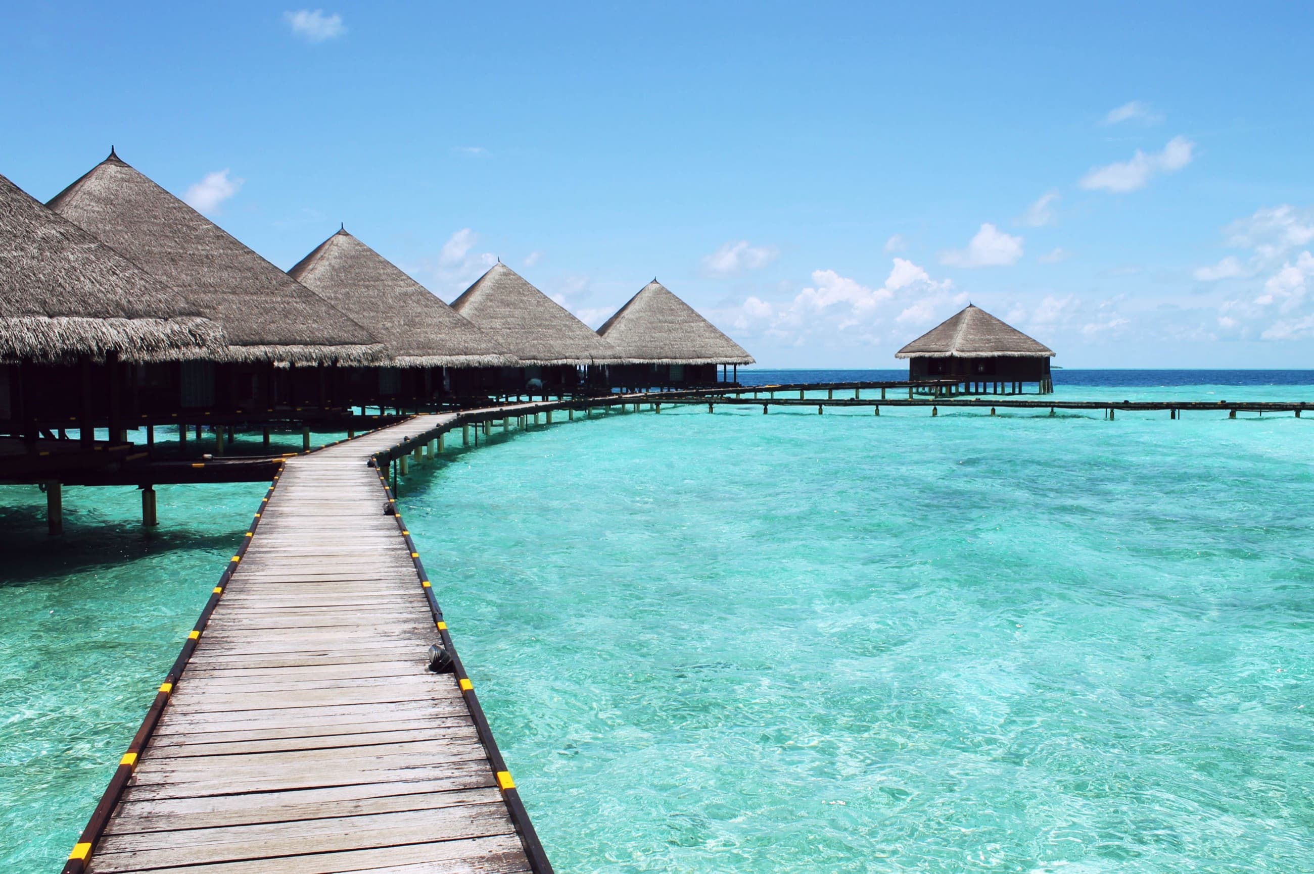 A wooden boardwalk connecting a row of thatched overwater bungalows