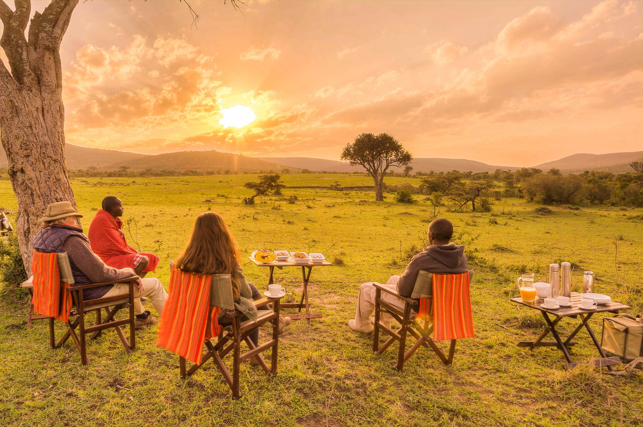 A Maasai guide sharing a bush breakfast with guests as the sun rises over the Mara