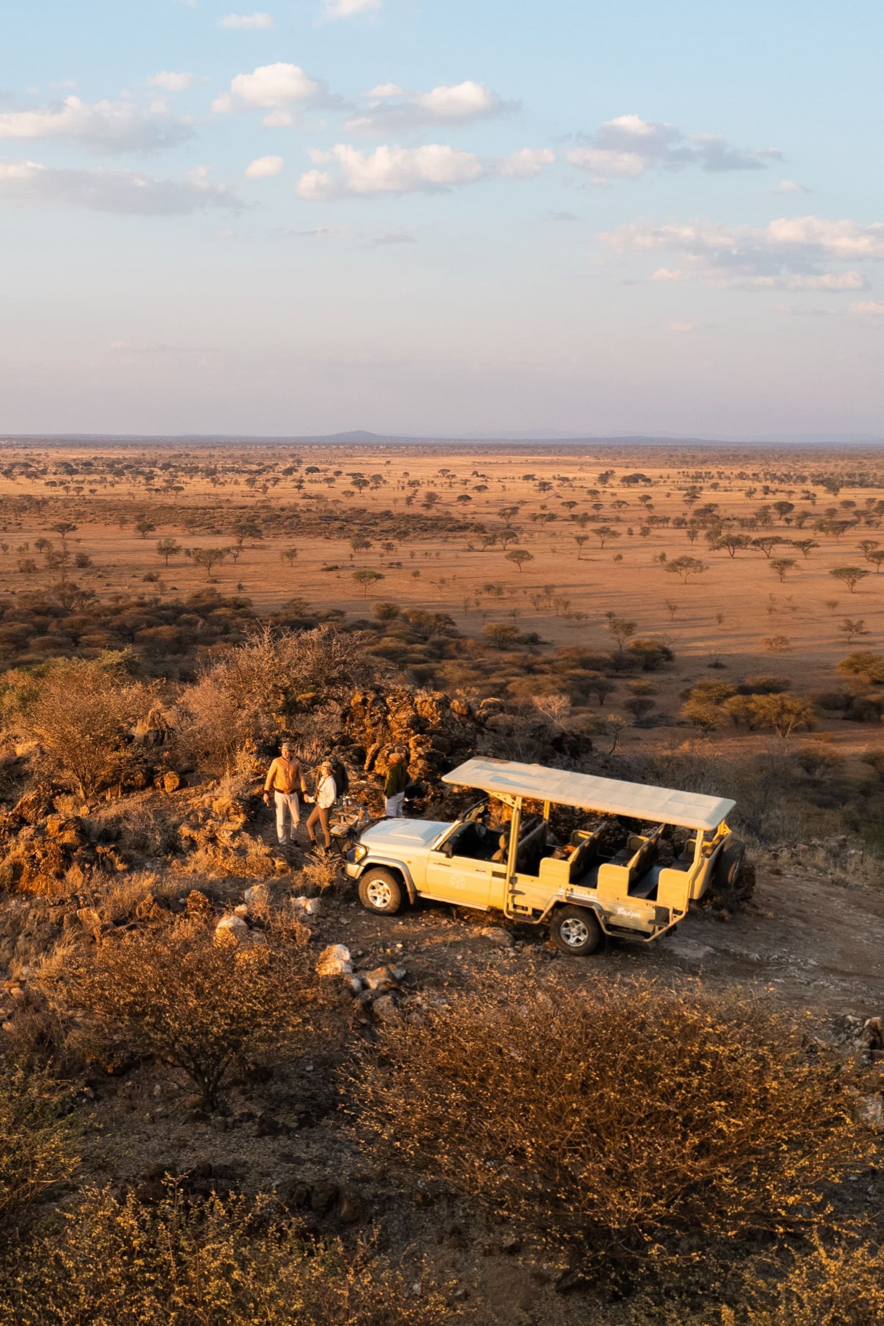 Safari vehicle and guests on a rocky escarpment overlooking the Rift Valley