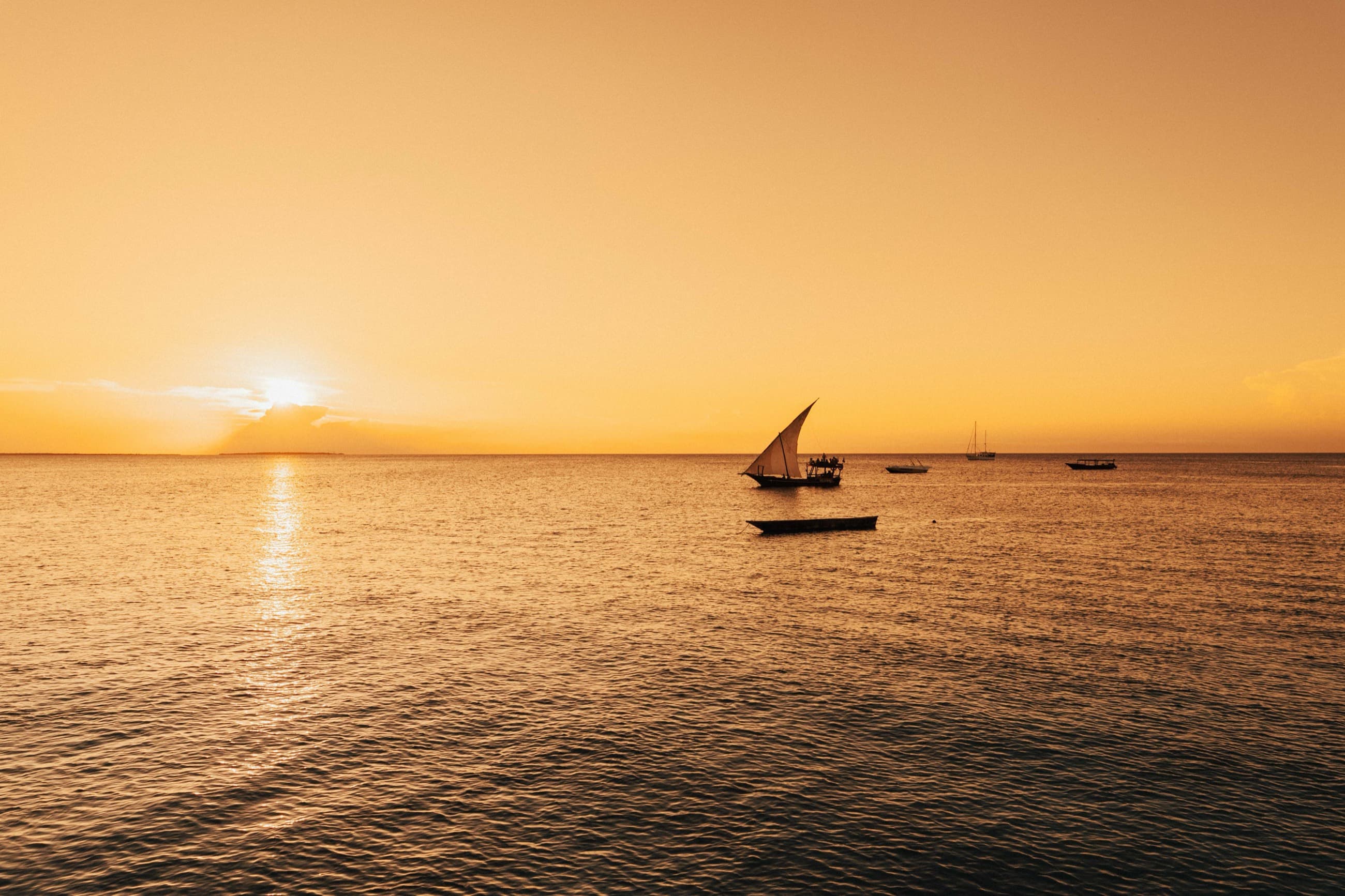 A traditional dhow under sail silhouetted against a golden sunset