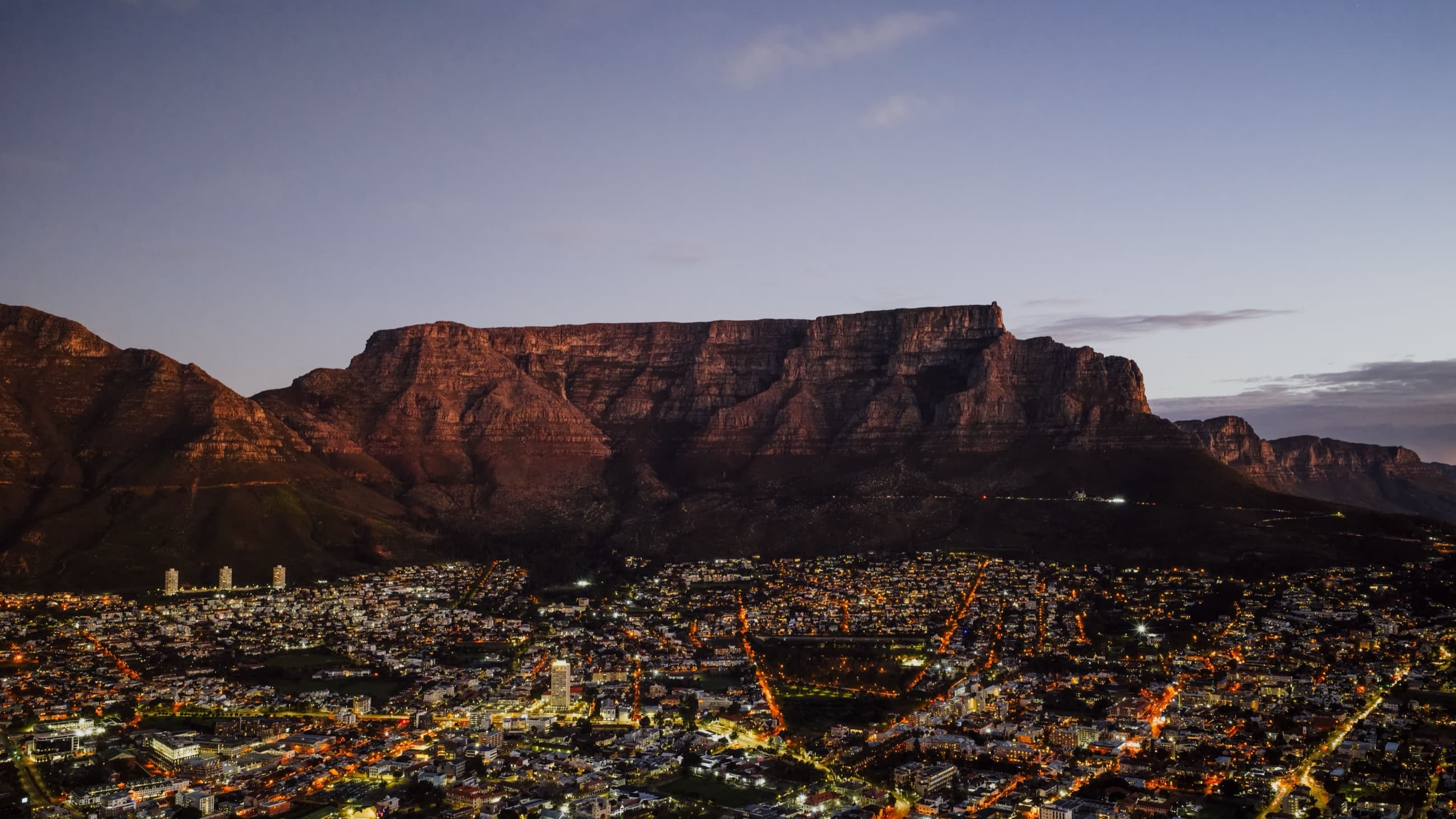 Table Mountain rising over Cape Town's city lights at dusk